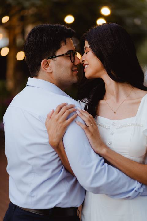 Noivos quase se beijando, sob luzes de varal, entardecer'