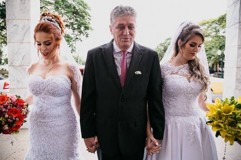 Casamento duplo, de gêmeas, noivas prontas para entrar na igreja, de mãos dadas com o pai'
