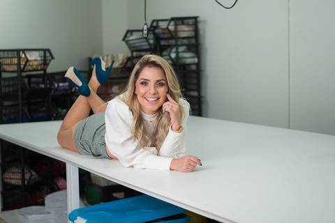 Retrato empresarial na empresa da empresária empreendedora Jhuliany, JB Robes Personalizados, foto dentro da fábrica, em cima da mesa de corte'