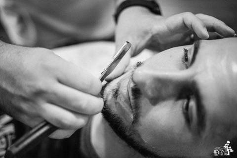 mão de barbeiro segurando navalha enquanto faz a barba do noivo'