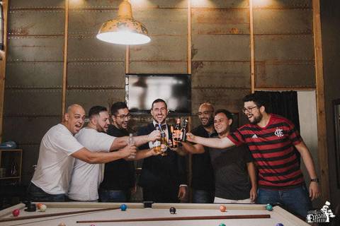 brinde do noivo com os padrinhos na frente de uma mesa de sinuca, com copos cheios de cerveja, em barbearia de maringá, durante o making of do noivo'