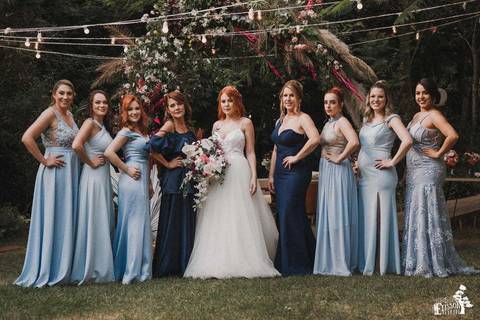 Noiva e madrinhas posando para foto, durante o dia, depois do casamento, em ambiente aberto e verde, mãe e sogra da noiva de vestido azul escuro e madrinhas de azul claro'