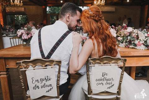 Noivos sentados de costas para a camera, com cadeiras e plaquinhas, depois do casamento ao ar livre, com decoração boho, em Maringá/PR'