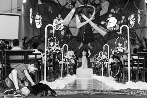 criança brincando com cachorro na porta da igreja durante o casamento, com os noivos no fundo'