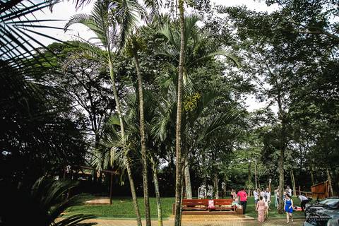 Fim de casamento, durante o dia, poucos convidados ainda no local, conversando e rindo, de longe'