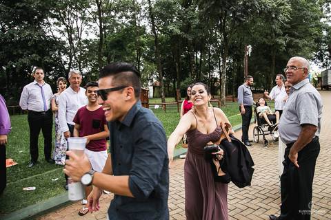 Fim de casamento, durante o dia, poucos convidados ainda no local, conversando e rindo, de longe'