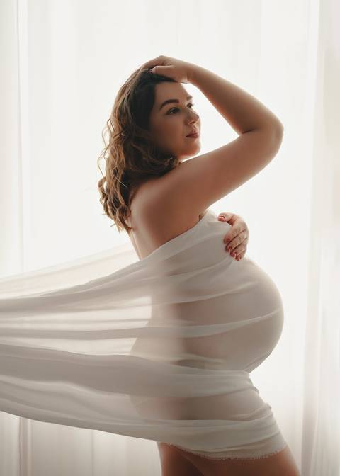 foto de gestante com tecido branco na janela '