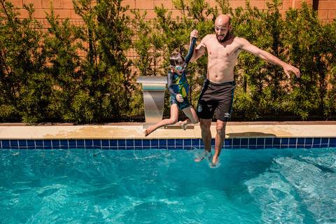pai pulando com filho na piscina'