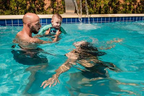 pai com filho no colo e mãe mergulhando na piscina'