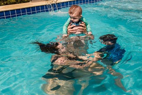 pai com filho no colo e mãe e filho mergulhando na piscina'