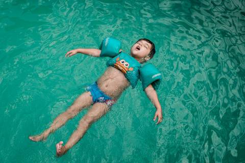 criança boiando na piscina'