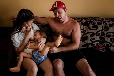 pai e mãe juntos enquanto o filho mama, sentados no sofá da sala '