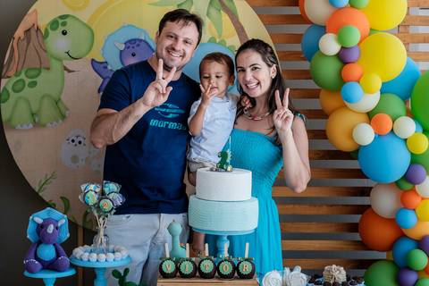 retrato dos pais com a criança no colo na mesa do bolo mostrando 2 anos com os dedos'