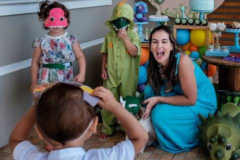 mãe sorrindo para o filho que está usando uma máscara de dinossauro'