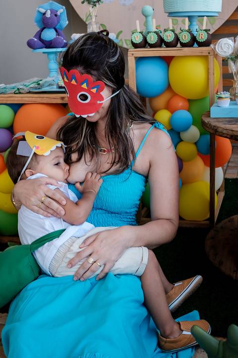 mão amamentando o filho em frente a mesa do bolo'