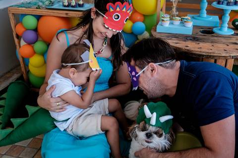 pai e mãe brincando com o filho sentados no chão em frente a mesa do bolo'