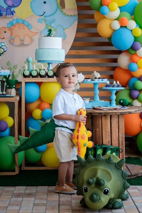 aniversariante com rabo de dinossauro em frente a mesa do bolo'