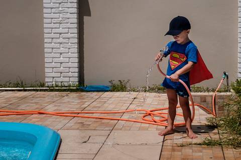 menino brincando com a mangueira de água na beira da piscina'