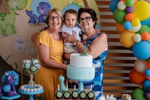 avós com o neto no colo atrás da mesa do bolo '