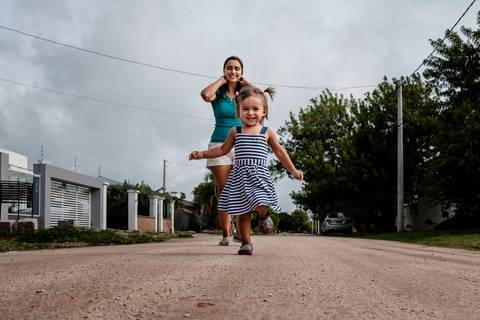 mãe e filha caminhando na rua em frente a casa'