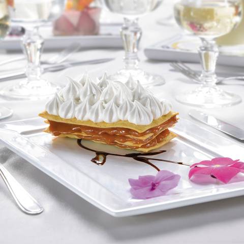 Fotografía publicitaria de José Chiodini que resalta un milhojas con capas de crema y merengue italiano, presentado con decoración floral y reducción de chocolate.'