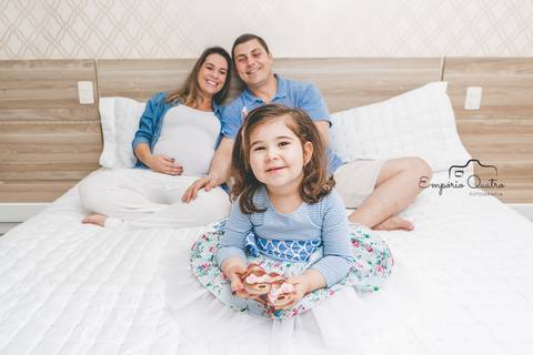 ensaio gestante família reunida na cama filha segurando sapatos do bebê'