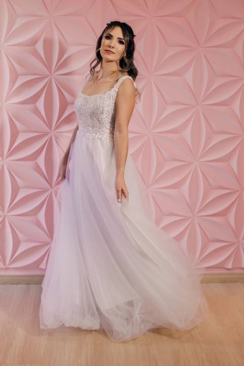 mulher posando pra foto de vestido branco em frente a parede rosa'