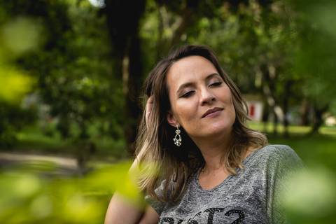 a gestante entre folhas verdes mexendo no cabelo e de olho fechado'