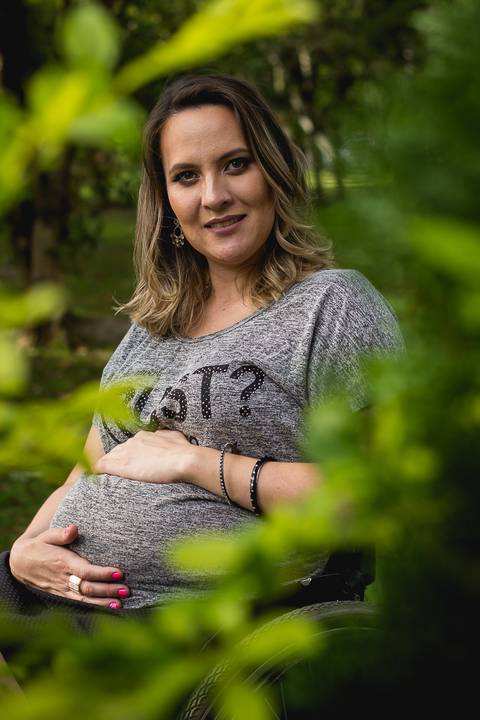a gestante entre as folhas verdes com a mão na barriga e sorrindo'