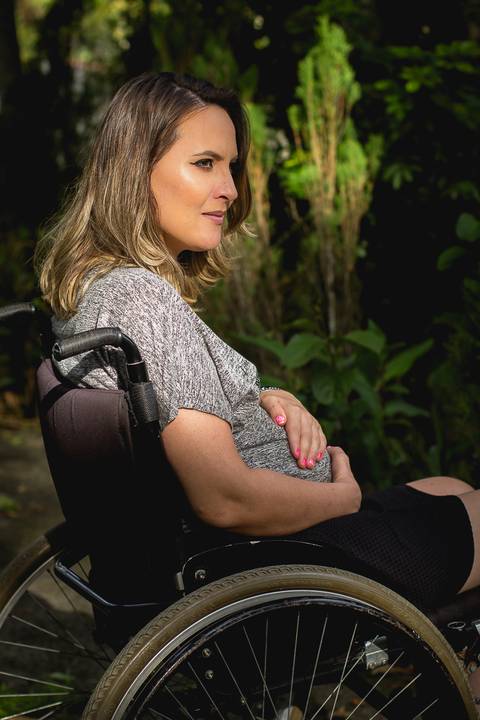 foto na vertical da gestante com a mão na barriga sob um feixe de luz do sol'