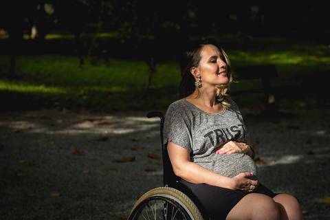 gestante cadeirante sorrindo sob um feixe de luz do sol'