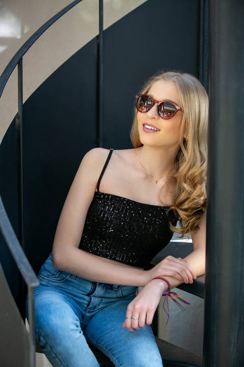ensaio 15 anos menina loira com roupas com calça jeans e blusa preta de paetê sentada em um escada caracol usado óculos escuros. Fábio Martins fotografo '