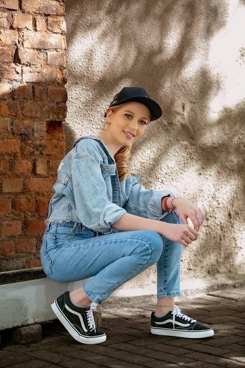 book de 15 anos menina loira com roupas jeans e blusa preta de paetê sentada na calçada com parede rustica ao fundo usado boné. Fábio Martins fotografo '