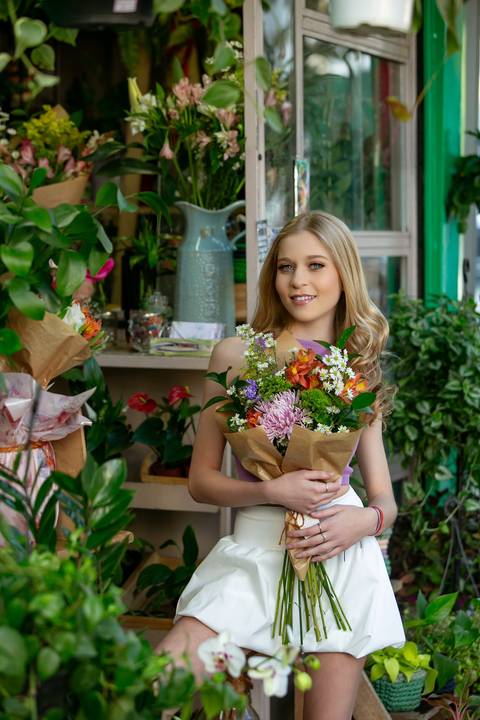 book de 15 anos menina loira com saia e tênis branca e blusa lilás em banca de flores estilo Londres  segurando boque. Fábio Martins fotografo '