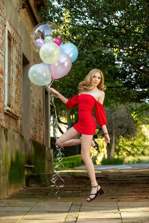 ensaio de 15 anos menina loira com vestido vermelho de alhos azuis encostada em um porta vintage com balões com gás na mão. Fábio Martins fotografo '