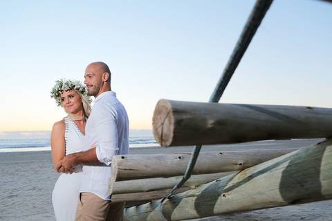 FOTOGRAFIA-NA-PRAIA-DE-GAROPABA-E-PRAIA-DO-ROSA-PRÉ-WEDDING-fotos-casal-na-praia-do-rosa-escada-de-tronco-mar-ao-fundo-por-do-sol-praia-de-garopada-praia-do-rosa-noiva-noivo-vestido-branco-conjunto-branco-loira-com-coroa-de-flores-noivos-casamento-praia'