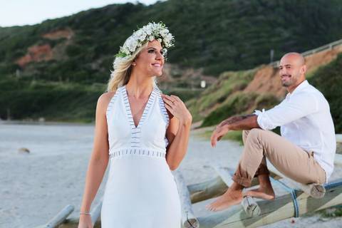 Fotos noivas com noivo ao fundo na praia do rosa. Noivo sentado FOTOGRAFIA-NA-PRAIA-DE-GAROPABA-E-PRAIA-DO-ROSA-PRÉ-WEDDING-fundo-noiva-frente-com-um-bela-coroa-de-flores-naturais-noivo-olhando-noiva-sentado-beira-praia-santa-catarina-noiva-sorrindo-foto'