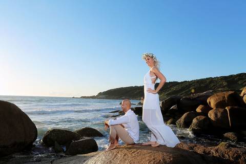 FOTOGRAFIA-NA-PRAIA-DE-GAROPABA-E-PRAIA-DO-ROSA-PRÉ-WEDDING-fotos-casal-na-praia-do-rosa-em-cima-de-pedra-com-o-mar-ao-fundo-pre-wedding-noiva-de-pe-noivo-sentado-nas-pedras-praia-de-santa-catarina-praia-de-sc-fotos-mar-sc-casamento-noiva-com-coroa-flores'