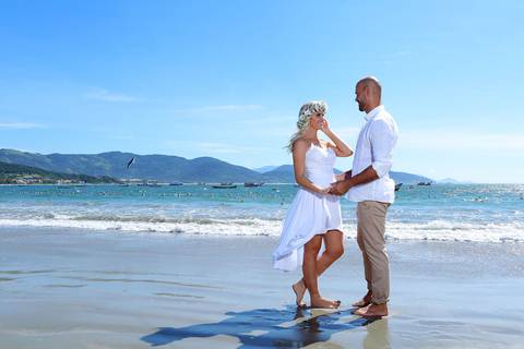fotos casal na areia com o mar azul ao fundo, noiva com vestido curto e coroa de flores naturais. '
