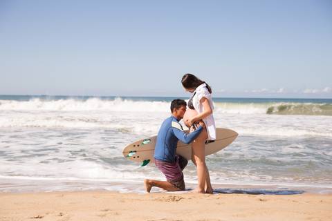 marido beijando a barriga da esposa na praia. ensaio gestante '