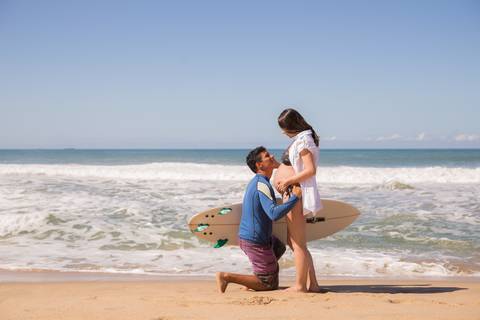marido beijando a barriga da esposa na praia. ensaio gestante '