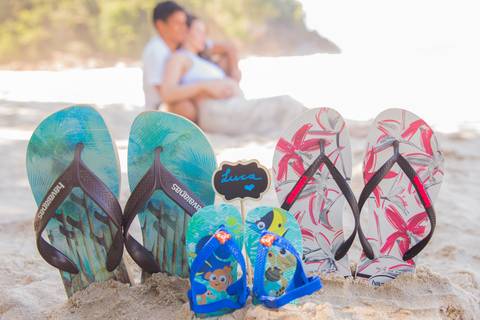 foto dos chinelos do casal e do bebê na areia. ensaio gestante'