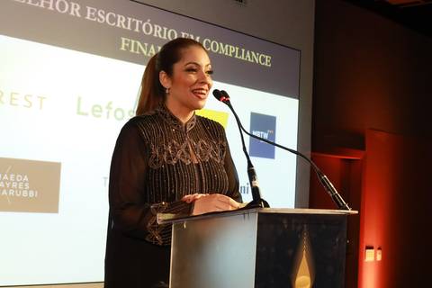Vencedora discursando no púlpito durante o BRALLAW 2023. Contrate um fotógrafo de eventos corporativos que captura com profissionalismo os discursos e a emoção dos momentos de premiação em São Paulo.'