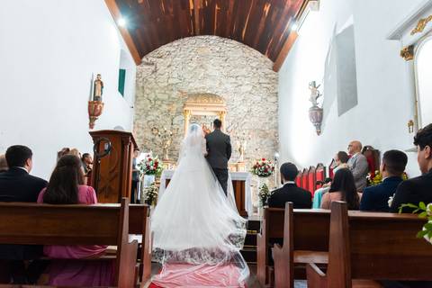 Visão do casal de costa no altar, calda longa do vestido de noiva'