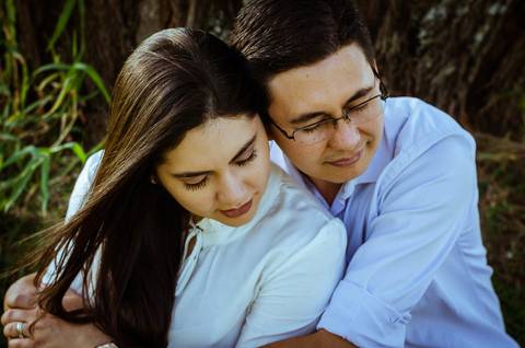 Ensaio fotográfico do casal. Esta foto eles se abraçam com carinho sentindo uma brisa suave. '