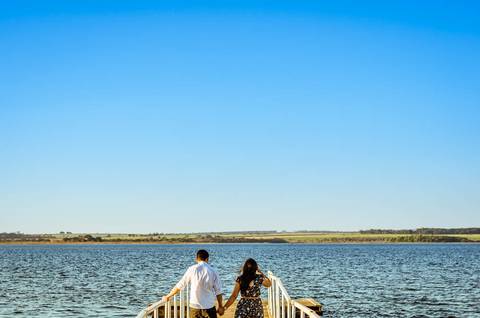 Fotografia do ensaio de casal caminhando em uma trapiche flutuante sob o rio Tietê e com céu azul.'