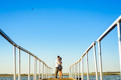 Fotografia do ensaio de casal se abraçando em uma trapiche flutuante sob o rio Tietê e com céu azul.'