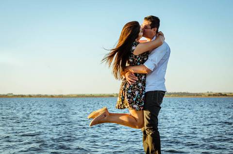 Fotografia do ensaio de casal se abraçando, ele a segura nos braços. Ao fundo está o rio Tietê.'