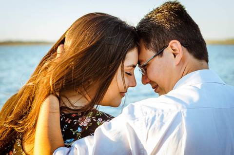 Foto do casal bem próximos com a luz do por do sol e o rio ao fundo.'