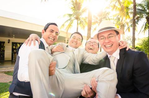 Fotografia de casamento com cerimônia e festa e recepção ao ar livre durante o dia no Califórnia Eventos em Araçatuba SP. Os amigos e irmão do noivo seguram ele, todos sorrindo muito.'